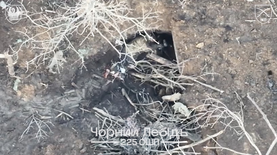 Unequipped Russian is hit with FPV in a tree line. With his legs severely wounded, he crawls to a foxhole with a bunch of munition lying around, grabs what looks like previously undetonated FPV and triggers exposion
