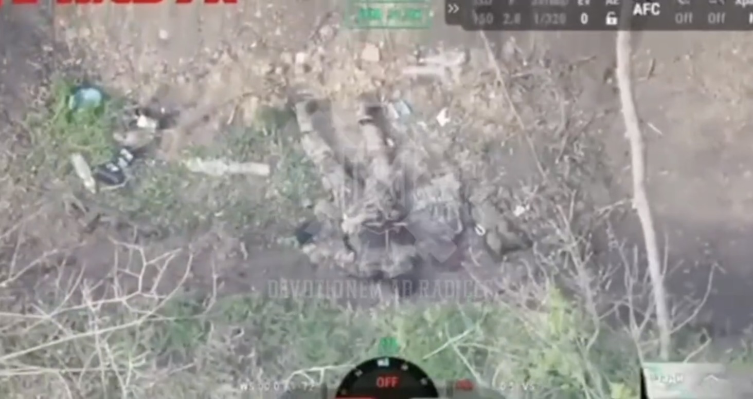 Russian with no helmet lies on his belly, unclear whether injured or not. He pulls the pin on his grenade and detonates it under his chest. Explosion is powerful enough to flip his body around