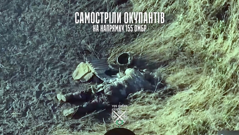 Russian soldier is lying by the side of a dirt road with his helmet and ballistic vest off, apparently injured. He pulls the pin on his grenade, and leaves it next to his head to detonate