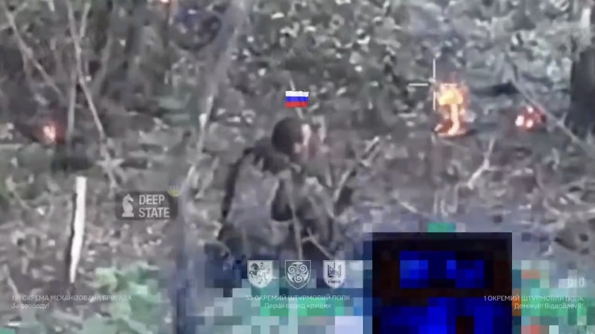 Fully equipped Russian with his helmet missing is seen from behind. He sits on the ground in what looks like drone strike aftermath with stuff burning around, and shoots himlesf from under his chin